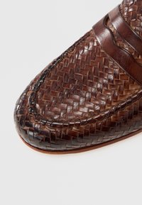 Καφέ πλεκτό δερμάτινο παπούτσι με λείο δερμάτινο λωρίδα στην κορυφή, στρογγυλεμένη μύτη και υφή στην επιφάνεια.