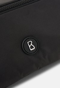 Funda de tela negra que presenta un logo plateado "B" sobre un fondo negro circular, con una textura suave y un cierre con cremallera en la parte superior.