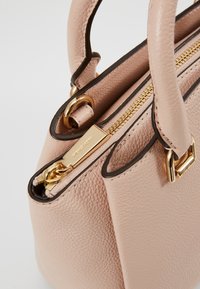 Sac à main en cuir beige texturé avec bordure noire, fermeture éclair et quincaillerie dorées, doté de deux poignées arrondies.