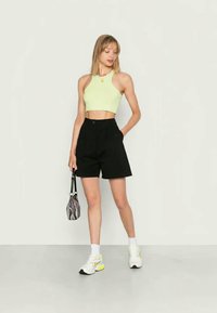 Top crop verde claro, calções pretos, sapatilhas brancas e amarelas, e uma pequena bolsa listrada em preto e branco, com um aspeto suave e casual.