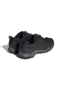 Zapatos deportivos negros con parte superior de tela texturizada, punta reforzada y suelas acolchadas. Presentan cordones elásticos y acentos metálicos.