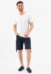 T-shirt bianco in cotone con scollo a V, pantaloni cargo blu navy con tasche laterali e scarpe slip-on blu navy. Tessuto morbido e design casual.