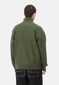 Sudadera de color verde oscuro con cuello alto, puños y dobladillo acanalados. Textura suave, ajuste relajado y detalle de costura mínima.