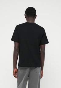 Camiseta negra de manga corta hecha de algodón, con un cuello redondo y un corte recto, acompañada de pantalones de mezclilla gris.