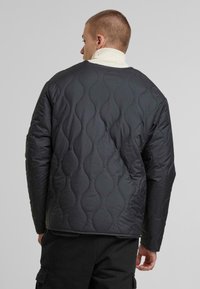 Quiltet sort jakke med bølgemønster, med rund krave og lange ærmer, lavet af glat, isoleret materiale.