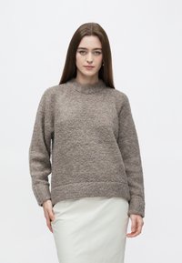 Brun texturerad tröja med långa ärmar, rund halsringning och avslappnad passform, kombinerad med en ljuskjol. Mjuk och mysig look.