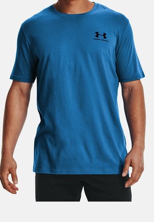 Camiseta de algodón azul, de manga corta, con cuello redondo y un pequeño logo negro de Under Armour en el pecho. Textura suave, corte casual.