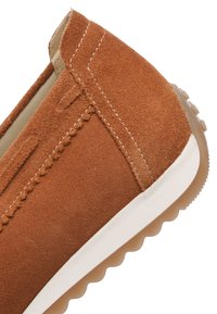Detailní záběr na hnědý semišový nazouvák s bílým prošitím a bílou podrážkou s texturovaným gumovým spodkem.