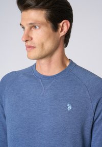 Felpa blu realizzata in tessuto morbido, con collo tondo, maniche raglan e un piccolo logo ricamato sul petto.