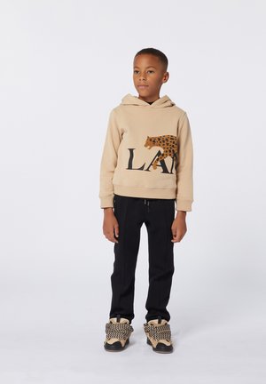 Felpa beige con stampa leopardata nera e lettere in grassetto sul davanti, abbinata a pantaloni neri e sneakers alte con dettagli intrecciati.