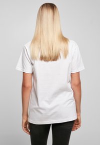 Hvit bomulls t-skjorte med korte ermer, avslappet passform og rett nederkant; brukt med mørke bukser; håret er langt og rett, sett fra bak.