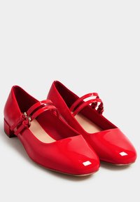 Punaiset lakatut ballerinat, joissa on pyöreä kärki, matala paksukanta ja kaksinkertainen remmi yksityiskohtana, joka on kiinnitetty soljilla. Sujuva, kiiltävä pinta.