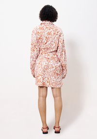 Robe courte à manches longues, motif floral orange et blanc, taille ceinturée et ourlet incurvé. Tissu lisse avec une texture légère.