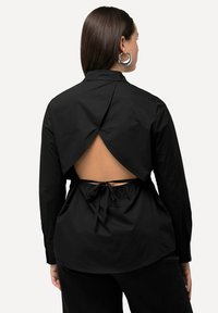 Maglietta nera a maniche lunghe con schiena bassa, dotata di un dettaglio in vita annodato e un design posteriore a strati. Tessuto liscio con una trama elegante.