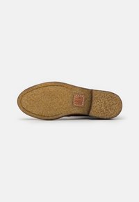 Brown shoe sole with a textured surface, featuring a slight curve at the toe and a rectangular logo patch near the heel. Synthetic material.
