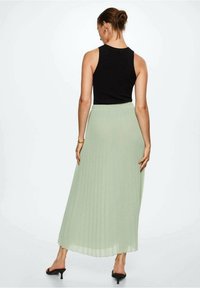 Falda midi verde plisada hecha de tela ligera, combinada con una camiseta sin mangas negra. Presenta una cintura elástica y llega hasta los tobillos.