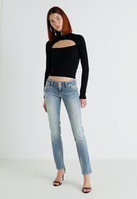 Black ribbed long-sleeve top with a cut-out detail, paired with light-wash denim jeans, featuring a straight leg and five-button closure.