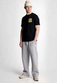 Sort bomulds t-shirt med et gult solgrafik på brystet, parret med lysegrå joggingbukser og en cremefarvet ribbet beanie.