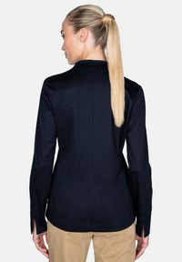 Marineblaue Langarmbluse mit rundem Kragen, seitlichen Schlitzen am Saum und einer glatten Textur. Getragen mit beigen Hosen.