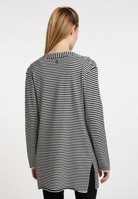 Černobíle pruhovaný top s dlouhým rukávem, bočními rozparky a kulatým výstřihem. Na zadní straně se nachází detail s knoflíkem. Měkká textilie.
