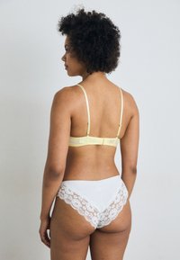 Yellow bra with adjustable straps and clasp closure; white panties with lace trim featuring floral pattern. Smooth texture, back view.