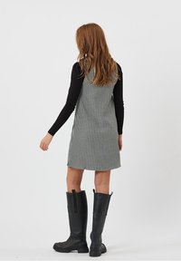 Robe à carreaux noirs et blancs avec une silhouette évasée, associée à des bottes en caoutchouc noires montant jusqu'aux genoux. Haut à manches longues visible en dessous.