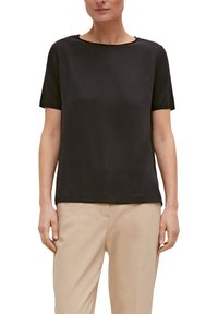 Czarny t-shirt z krótkim rękawem i okrągłym dekoltem, wykonany z gładkiego materiału. Nosi się go z jasnobeżowymi spodniami typu prosto nogawka o minimalnym wzornictwie.