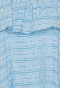 Tecido azul claro com uma textura rugosa e finas riscas verticais e horizontais em azul mais escuro. Parte de um design com volantes na parte superior.