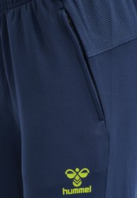 Marina idrottsshorts med en blixtlåsficka, texturerad midja och en klar gul hummel-logotyp på det nedre benet. Tillverkade av ett ventilerande material.