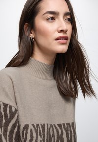 Beiger Pullover mit geripptem Hochkragen; verfügt über ein dunkelbraunes Tiermuster im unteren Bereich; weicher, strukturierten Strickstoff.