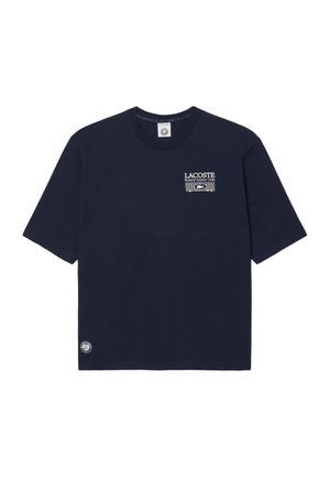 Camiseta de manga corta azul marino con el texto y logo "Lacoste Roland Garros Club" en el pecho y un pequeño logo circular cerca del dobladillo.