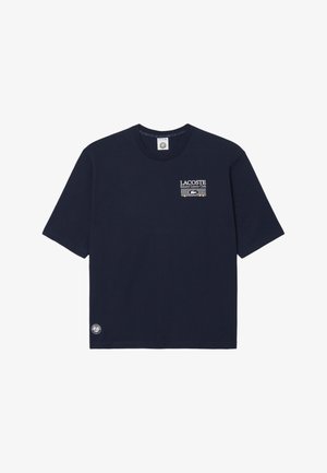 Camiseta de manga corta azul marino con el texto y logo "Lacoste Roland Garros Club" en el pecho y un pequeño logo circular cerca del dobladillo.