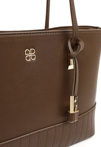 Brown leather tote bag with gold-tone logo, gold accents on strap ends, and textured horizontal stitching at the bottom center.