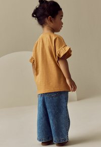 Gelbes strukturiertes Hemd mit kurzen Rüscheärmeln, kombiniert mit weit geschnittenen blauen Jeans. Schlichtes Design, tailliert, lässiger Stil.