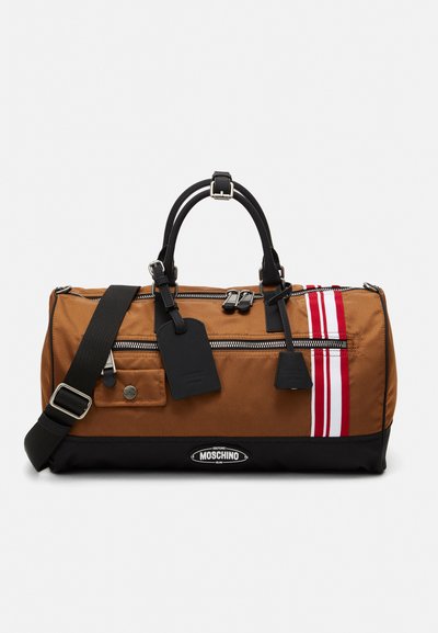 Brown nylon duffel bag with black accents, silver hardware, zippered pockets, two red stripes, and a logo patch; features adjustable strap and handles.