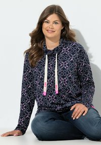 Marinblå tröja med mönster och rosa detaljer, polokrage och dragsnören. Mjuk tyg, långa ärmar och avslappnad passform som möter mörka jeans.