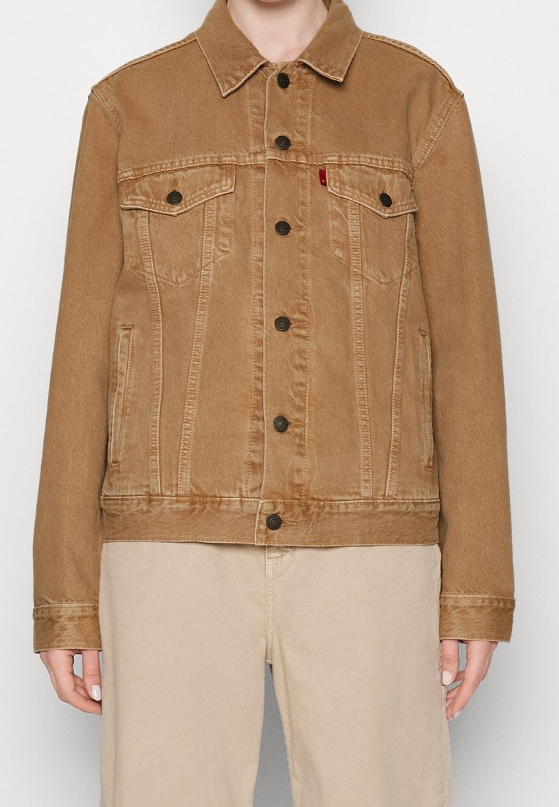 Chaqueta de mezclilla marrón con cierre de botones en la parte delantera, dos bolsillos en el pecho, bolsillos laterales y un collar puntiagudo; presenta una textura desgastada para un aspecto vintage.