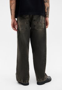 Mørkegrønne, brede jeans med en falmet tekstur, to baglommer og kontrasterende syninger. Båret med sorte sko.