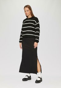 Schwarz-weißer gestreifter Pullover mit Rundhalsausschnitt, kombiniert mit einem schwarzen Maxirock mit seitlichen Schlitzen und schwarzen Plateauschuhen mit Socken.