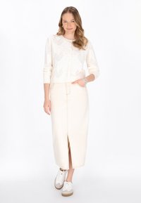 Maglione lavorato a maglia di colore crema con motivi geometrici, abbinato a una gonna di jeans beige chiaro con uno spacco frontale e scarpe da ginnastica bianche.