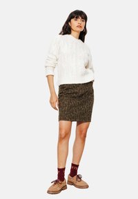 Pull en tricot blanc avec motif en relief, associé à une jupe moulante à imprimé léopard olive. Chaussures à lacets brunes et chaussettes bordeaux.