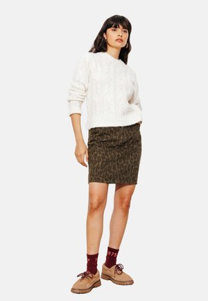 Pull en tricot blanc avec motif en relief, associé à une jupe moulante à imprimé léopard olive. Chaussures à lacets brunes et chaussettes bordeaux.