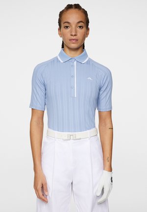 Lichtblauw polo-shirt met korte mouwen, verticale ribbels en een witte kraag. Heeft een subtiele logo op de borst en is gecombineerd met witte broek.