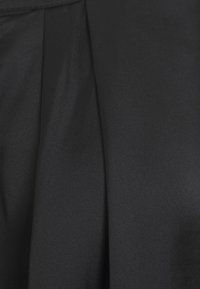 Svart veckat tyg med en sl ät textur, som har en subtil lyster och skarpa veck. Materialet verkar lätt och flödar.