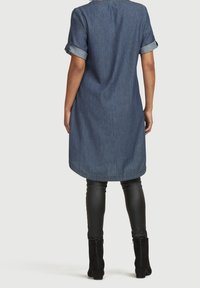 Denimklänning med uppvikt ärmar, med längd till mitten av låret, böjd nederkant, samt i kombination med svarta PU-läderleggings och stövlar med ankellängd.