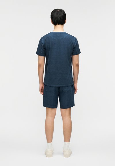 Μπλε βαμβακερό μπλουζάκι με κοντά μανίκια και στρογγυλή λαιμόκοψη, σε συνδυασμό με μπλε σορτς που διαθέτουν δύο πίσω τσέπες. Και τα δύο ρούχα έχουν υφή.