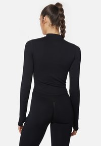 Musta pitkähihaine paita korkealla kauluksella, istuva malli ja sileä rakenne. Yhdistetty mustiin korkeavyötäröisiin leggingseihin, luoden saumatonta ilmettä.