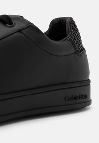 Crne kožne tenisice s teksturiranim petama, okruglim vrhom i tonovima šavova. Ima suptilan Calvin Klein logo sa strane.