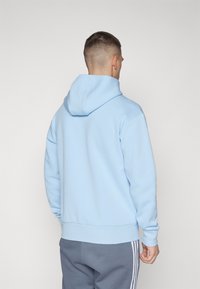 Felpa blu chiaro con tasca a canguro, cappuccio regolabile e polsini a coste. Abbinata a pantaloni da tuta grigi con strisce bianche sui lati.