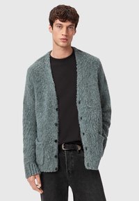 Teksturowany, jasnoniebieski kardigan z otwartym przodem, długimi rękawami i dwiema przednimi kieszeniami, z czarnymi guzikami i luźnym krojem.